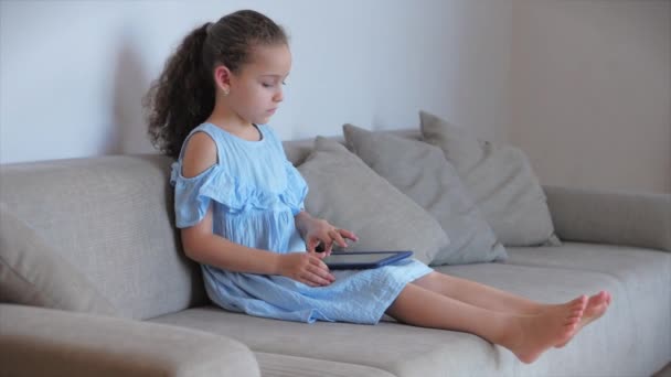 Щаслива маленька дівчинка або дитина, що грає вдома, розслабляючись, використовують смартфон, що сидить на дивані дочка і син, дивіться на екрані мобільного телефону, дивіться мультфільми . — стокове відео
