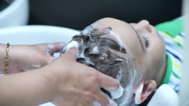 Parekhmacher, po strzyżeniu dziecka w wieku przedszkolnym, umyć włosy, mydło z szamponem, dziecko leży odpoczynku i cieszy się podczas mycia włosów po ich strzyżeniu. — Wideo stockowe