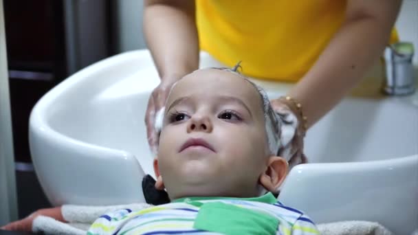 Parekhmacher, po strzyżeniu dziecka w wieku przedszkolnym, umyć włosy, mydło z szamponem, dziecko leży odpoczynku i cieszy się podczas mycia włosów po ich strzyżeniu. — Wideo stockowe