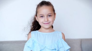 Portre Komik küçük kız kameraya bakarak gülümsüyor. Evdeki kanepede oturuyor. Güzel yüzlü şirin çocuk sınıfa parmak kaldırıyor. Mutlu bir çocukluk kavramı.