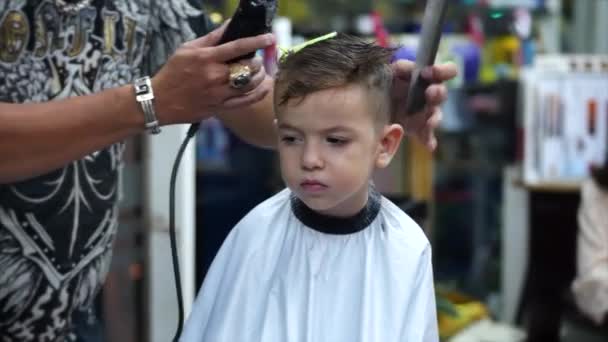 Taglio di capelli per bambini nel salone al momento dell'epidemia di coronavirus.Bambino ottiene un taglio di capelli.Stylist in una maschera protettiva da covid-19 rende un'acconciatura elegante. — Video Stock