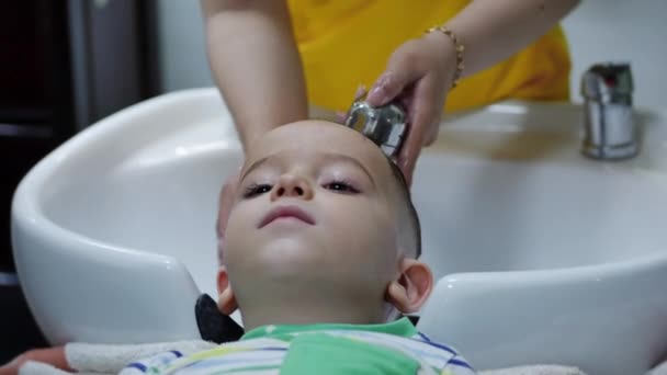 Parekhmacher, nach dem Haareschneiden ein Kind im Vorschulalter, waschen ihre Haare, Seife mit Shampoo, Kind liegt und genießt, während sie ihre Haare waschen, nachdem sie ihre Haare geschnitten haben.Kinderhaarstyling — Stockvideo