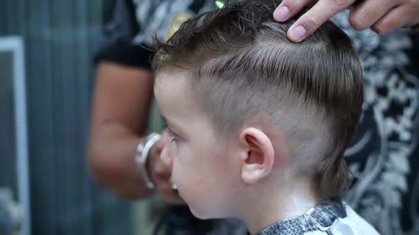 Childrens haircut in the salon at the time of the coronavirus epidemic.Little boy gets a haircut.Stylist in a protective mask from covid-19 makes a stylish hairstyle. — Stock Video