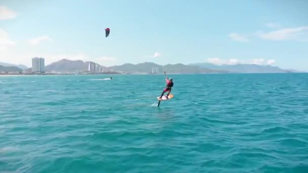 Vue aérienne de la plage de la ville et des personnes actives pratiquant le kite surf et la planche à voile. Lieu de kitesurf, concept sportif, mode de vie sain, vol humain. — Video