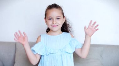 Gülümseyen komik küçük bir kızın portresi. Sakin ol, kameraya bak, el salla. Evdeki kanepede oturan bir blogcu olarak merhaba, şirin yüzlü şirin bir çocuk sofshaw başparmağında oturuyor.