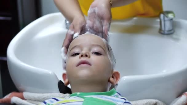 Parekhmacher, après avoir coupé les cheveux d'un enfant d'âge préscolaire, se laver les cheveux, savon avec shampooing, enfant se couche au repos et profite pendant qu'ils se lavent les cheveux après qu'ils ont leur coupe de cheveux. — Video