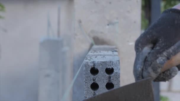 Cerca de tiro en las manos albañiles, trabajador voluntario masculino pone ladrillo en la pared con cemento usando paleta, constructor hombre pone los ladrillos, utilizando una cuerda estirada para un nivel uniforme de materiales de mampostería . — Vídeos de Stock