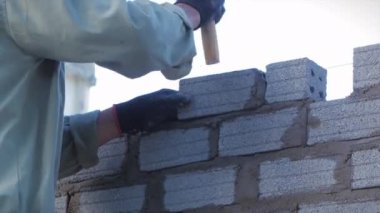 Tuğla ustalarının ellerine yakın çekim, erkek gönüllü işçi tuğlayı betonla duvara seriyor, mala kullanıyor, inşaatçı tuğlaları yerleştiriyor, esnek bir ip kullanarak duvarcılık malzemelerini dengeliyor..