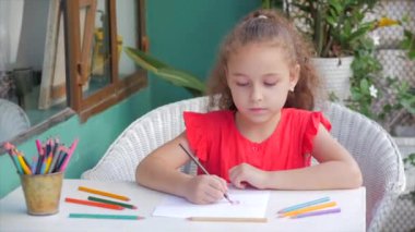 Evde tek başına resim çizen sevimli küçük kız ressam evde oturur ve kağıt rengi kalemlere resim çizer. İlköğretim odaklı çocuk resimleri çizer.