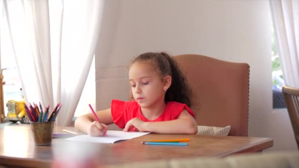 Glad liten flicka eller söt grundskolebarn i åldern 7-8 år hemma avkopplande sitter i huset och färger på papper använda färgpennor. Barn drar, fokuserade barn grundläggande utbildning koncept. — Stockvideo