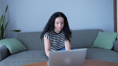 Genç Ciddi Kadın Laptop 'ta çalışıyor, evdeki koltukta oturuyor, iş kadını evde oturuyor dizüstü bilgisayarla ya da akıllı telefon kontrolleriyle evde çalışmak için posta kontrol ediyor..