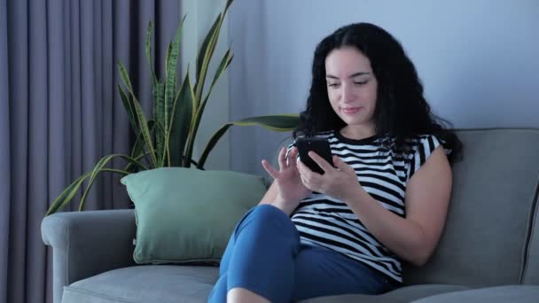 Mulher digitando no telefone sentado no sofá em casa, empresária senta-se em tipos de casa no smartphone verifica e-mail para estudar o trabalho on-line em casa. — Vídeo de Stock