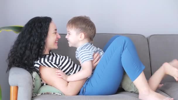 Heureuse famille saine jeune maman étreint mignon petit enfant fils qui embrasse mère sur les lèvres ou la joue assis sur le canapé à la maison, drôle mère et fils enfant garçon amour. — Video