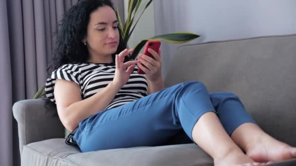 Nő gépelés telefonon ül a kanapén otthon, üzletasszony ül otthon típusok okostelefon ellenőrzi mail tanulni online munka otthon. — Stock videók