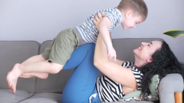 Lycklig frisk familj ung mamma kramar söt liten barn son som kysser mamma på läppar eller kind sitter på soffan hemma, rolig mor och son pojke kärlek. — Stockvideo