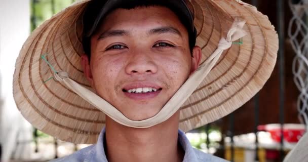 Porträtt av en ung asiatisk man i vietnamesisk hatt, mannen står och ler och tittar på kameran på gatan. — Stockvideo
