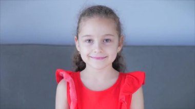 Portre Komik küçük kız kameraya bakıyor evde kanepede oturuyor, güzel yüzlü şirin çocuk kanepede oturuyor. Mutlu bir çocukluk kavramı.