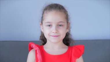 Portre Komik küçük kız kameraya bakıyor evde kanepede oturuyor, güzel yüzlü şirin çocuk kanepede oturuyor. Mutlu bir çocukluk kavramı.