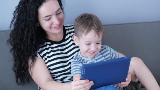 Happy family,mom and cute little children watch the phone,mom plays with children at home,relaxing using a smartphone,hugging,sitting on the couch, laughing, having fun,enjoying moments of family life — Stock Video