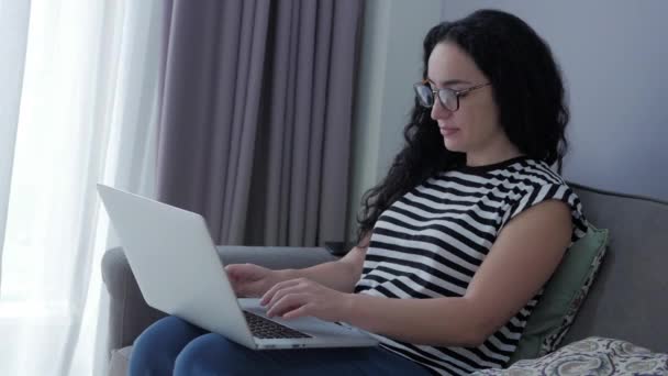 Femme tapant sur un ordinateur portable assis sur un canapé à la maison, femme d'affaires s'assoit à la maison types sur smartphone chèques mail pour étudier le travail en ligne à la maison. — Video