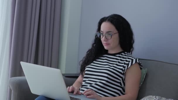 Mujer escribiendo en el ordenador portátil sentado en el sofá en casa, mujer de negocios se sienta en los tipos de casa en cheques de teléfonos inteligentes correo para estudiar el trabajo en línea en casa. — Vídeos de Stock