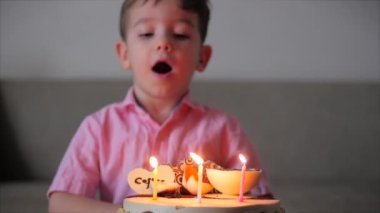 Dört çocuk kanepede oturup doğum günü pastasındaki yanan mumlara bakar, doğum günü dileği diler, doğum gününü ailesiyle kutlar ve pastadaki mumları söndürür..