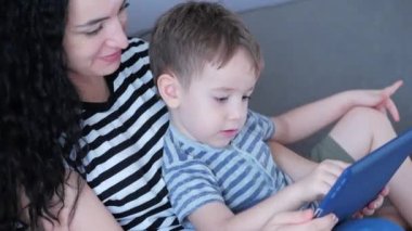 Mutlu aile, anne ve şirin çocuklar telefonu izliyor, anneleri evde çocuklarla oynuyor, akıllı telefon kullanıyor, sarılıyor, kanepede oturuyor, gülüyor, eğleniyor, aile hayatının tadını çıkarıyor.