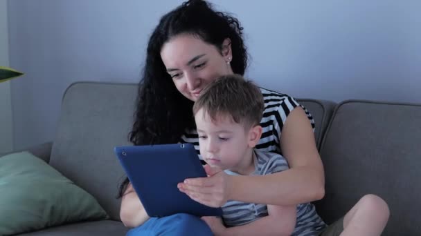 Familia feliz, mamá y niños pequeños y lindos ven el teléfono, mamá juega con los niños en casa, relajarse con un teléfono inteligente, abrazos, sentarse en el sofá, reír, divertirse, disfrutar de momentos de la vida familiar — Vídeo de stock