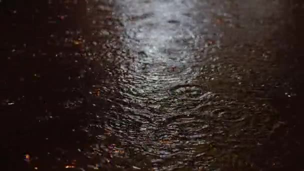 Des gouttes d'été ou d'automne de pluie d'eau tombent sur l'asphalte dans la ville se transformant en une grande flaque d'eau, inondant la rue. Les inondations sont la saison des pluies et de fortes pluies. Gouttes de pluie. — Video