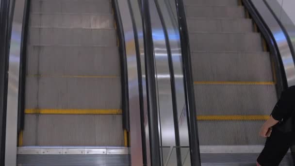 Subiendo por las escaleras mecánicas con lados de vidrio y pasos de metal. Escalera móvil en el centro comercial. Vista de cerca. La gente de la máscara Covid-19. — Vídeo de stock