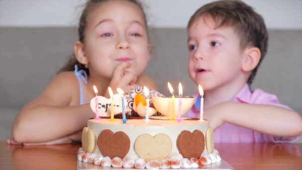 Menina bonito feliz e seu irmãozinho sentado no sofá fazendo um desejo de seu aniversário, comemorando o aniversário com a família, fazendo um desejo e soprando as velas no bolo . — Vídeo de Stock