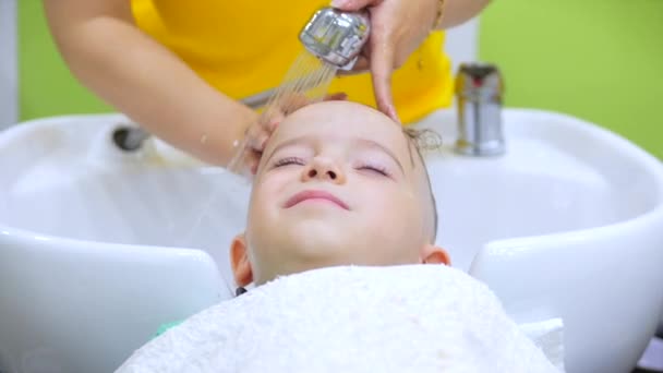 Parekhmacher, après avoir coupé les cheveux d'un enfant d'âge préscolaire, se laver les cheveux, savon avec shampooing, enfant se couche au repos et profite pendant qu'ils se lavent les cheveux après qu'ils ont leur coupe de cheveux. — Video