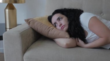 Yorgun, sıkılmış ya da yorgun genç bir kız ya da kadın depresyonda ve evdeki kanepede uzanıyor, üzgün gözlerle başka yere bakıyor, umutsuz bir bakış..