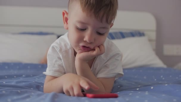 휴대 전화나 디지털 태블릿 기술 기기를 사용하는 취학 전 아동은 전화기처럼 보이고, 소파에 누워서 쉬고 있는 전화 안에서 놀고 있습니다. 아동 기술 중독 컨셉트는 집에서 게임을 합니다.. — 비디오