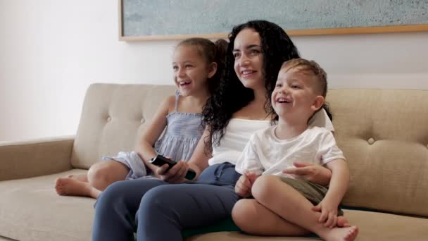 Família feliz, mamãe e crianças pequenas bonitos assistir a TV, mamãe brinca com as crianças em casa, relaxando usando uma casa de TV, abraçando, sentado no sofá, rindo, se divertindo, desfrutando de momentos da vida familiar — Vídeo de Stock