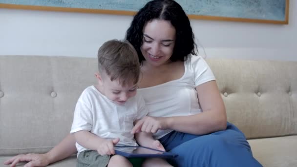 Gelukkig gezin, moeder en leuke kinderen spelen spelletjes tablet of laptop, moeder kijken met kinderen thuis, ontspannen met behulp van tablet, knuffelen, zitten op de bank, lachen, plezier hebben, genieten van momenten van familie — Stockvideo