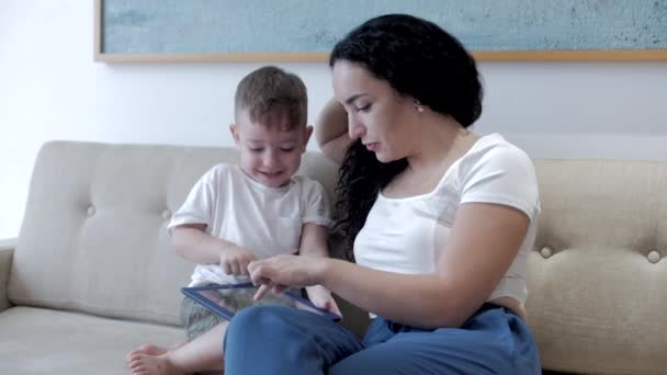 Glückliche Familie, Mutter und süße Kinder schauen Tablet oder Laptop, Mutter spielt mit Kindern zu Hause, entspannt mit Tablet, umarmt, sitzt auf der Couch, lacht, hat Spaß, genießt Momente des Familienlebens. — Stockvideo