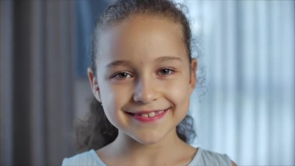 Portrét Legrační holčička usmívající se dítě dívající se do kamery sedí doma na gauči, roztomilé dítě s hezkou tváří sedí na pohovce. Koncept šťastného dětství. — Stock video