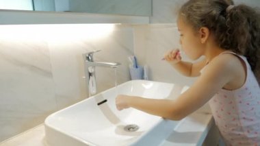 Banyoda dişlerini fırçalayan beyaz, güzel bir genç kız portresi. Çocuk günlük sağlık hizmeti rutini. Beyaz dişli çocuk aynaya bakıyor. Gülümseyen Yaşam Tarzı.