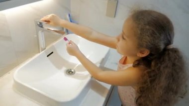 Banyoda dişlerini fırçalayan beyaz, güzel bir genç kız portresi. Çocuk günlük sağlık hizmeti rutini. Beyaz dişli çocuk aynaya bakıyor. Gülümseyen Yaşam Tarzı.