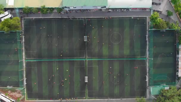 Edzés megkezdése egy focimeccs előtt. Játékmenet. Légi felvétel egy kis focipályáról, sok csapat focizik a szabadban, felülnézetből. Zöld mező jelölésekkel, labdával futó játékosok — Stock videók