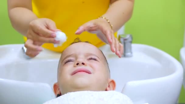 Parekhmacher, nach dem Haareschneiden ein Kind im Vorschulalter, waschen ihre Haare, Seife mit Shampoo, Kind liegt und genießt, während sie ihre Haare waschen, nachdem sie ihre Haare geschnitten haben.Kinderhaarstyling — Stockvideo