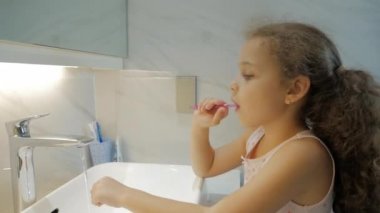 Banyoda dişlerini fırçalayan beyaz, güzel bir genç kız portresi. Çocuk günlük sağlık hizmeti rutini. Beyaz dişli çocuk aynaya bakıyor. Gülümseyen Yaşam Tarzı.