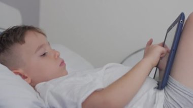 Telefon ya da dijital tablet teknolojisi kullanan şirin bir çocuk telefona bakar, koltukta tek başına dinlenir. Evde çocuk teknoloji bağımlılığı oyunu oynar..