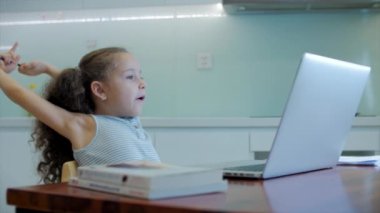 Küçük kız, 7-8 yaşlarında, evde eğitim gören sevimli bir ilkokul çocuğu, evde ders dinliyor, ev ödevlerini evden çıkmadan yapıyor. Çocuk eğitimi, çocuk eğitimi konsepti.