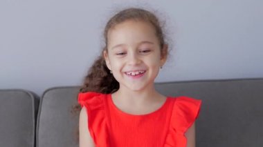 Portre Komik küçük kız kameraya bakarak evde kanepede oturuyor, tatlı yüzlü anaokulu çocuğu kanepede oturuyor. Mutlu Çocukluk kavramı.