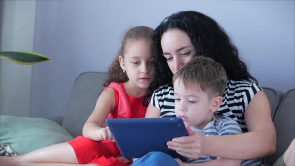 快乐的家庭，妈妈和可爱的孩子们一起看手机，妈妈在家里和孩子们玩耍，用智能手机放松，拥抱，坐在沙发上，大笑，开心，享受家庭生活的时刻 — 图库视频影像