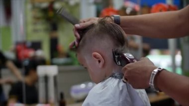 Küçük çocuk saçını kestiriyor. Çocukların saç şekillendirmesi. Covid-19 'un koruyucu maskeli stilisti şık bir saç stili yapıyor. Coronavirüs salgını sırasında kuaförde çocukların saç kesimi vardı..