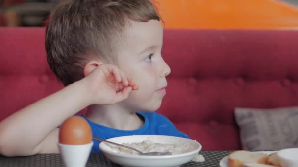 有趣的孩子吃粥加牛奶。小家伙很享受他的粥妈妈擦着嘴和脸看着可爱的男婴.一个迷人的孩子的笑声和母亲的尖叫声. — 图库视频影像