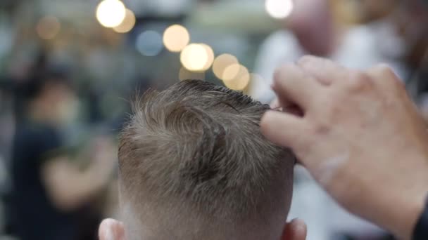 Kinderfrisur im Salon, Ein kleiner Junge bekommt eine Frisur beim Friseur. Kinderstyling. Eine Stylistin mit Covid-19-Maske trägt eine stylische Frisur. — Stockvideo